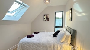A bedroom with a skylight, a bed with white bedding, a wooden floor, and a small bedside table with a lamp. - Stylish & Spacious Apartment (Tunbridge Wells)