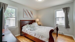 Una camera da letto con un letto di legno, un comodino con una lampada, un quadro appeso al muro e una finestra con tende.