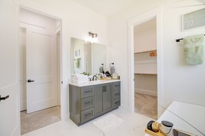A modern bathroom with a grey vanity, white sink, and a large mirror. There is a towel rack with a green towel and a framed sign on the wall. - Modern Houston Home w/ Yard, 3 Mi to Toyota Center (Houston)