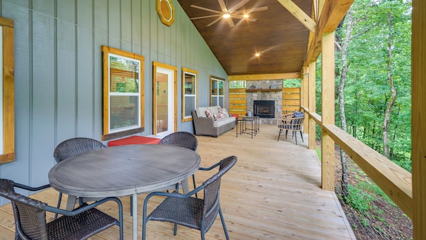 A covered deck with a dining area, a fireplace, and a view of the surrounding forest. - Blue Ridge Mountainside Cottage w/ Fire Pit! (Epworth)