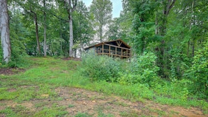 A cabin in a forest with a wooden structure, surrounded by dense trees and greenery. - Blue Ridge Mountainside Cottage w/ Fire Pit! (Epworth)