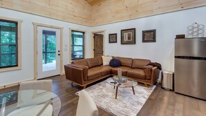 A modern living room with a brown leather sectional sofa, a glass coffee table, and a stainless steel refrigerator. - Blue Ridge Mountainside Cottage w/ Fire Pit! (Epworth)