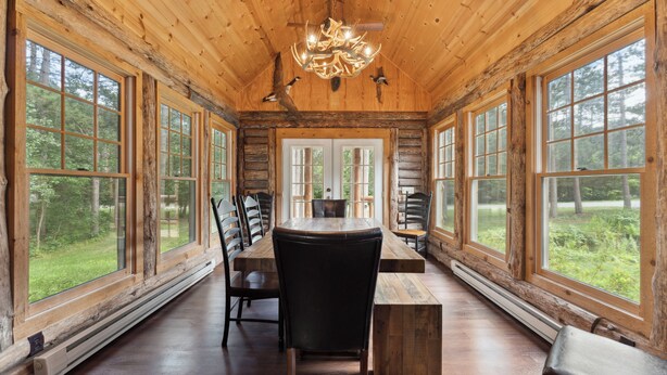 A rustic wooden cabin interior with a large dining table, chairs, and a chandelier.