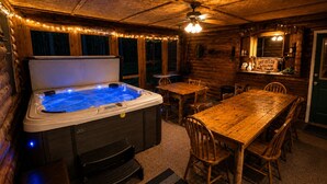 A wooden cabin with a hot tub, wooden dining table, chairs, and a bar area.