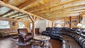 A log cabin interior with a wooden ceiling, leather sofas, a round coffee table, and a fireplace.