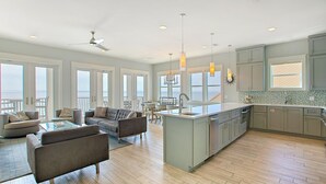A spacious living area with a large island kitchen, modern furniture, and large windows offering views of the ocean. - Dos Casas - Gulf-front Home with 2 Martini Pools and Beach Service (Destin)
