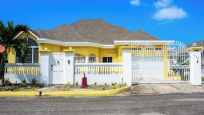 Una casa amarilla con entrada protegida por un portón, cerca blanca y buzón rojo.