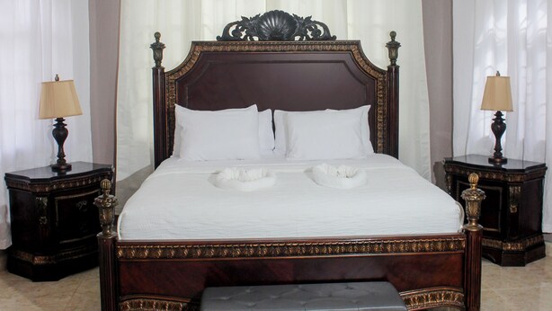 Una cama grande con cabecera de madera, dos mesitas de noche y un banco al pie de la cama.