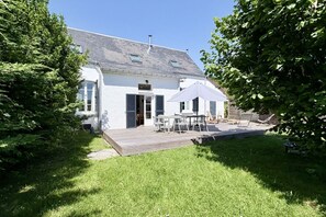 Une maison blanche avec une terrasse, une table entourée de chaises et un espace abrité.