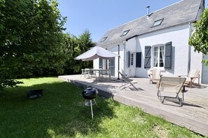 Une maison avec une terrasse, du mobilier d’extérieur et un barbecue.