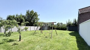 A grassy backyard with a swing set, a small tree, and a brick wall.