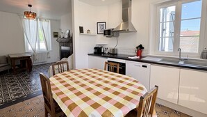 A modern kitchen with white cabinets, a stainless steel range hood, a dining table with a checkered tablecloth, and a large window.