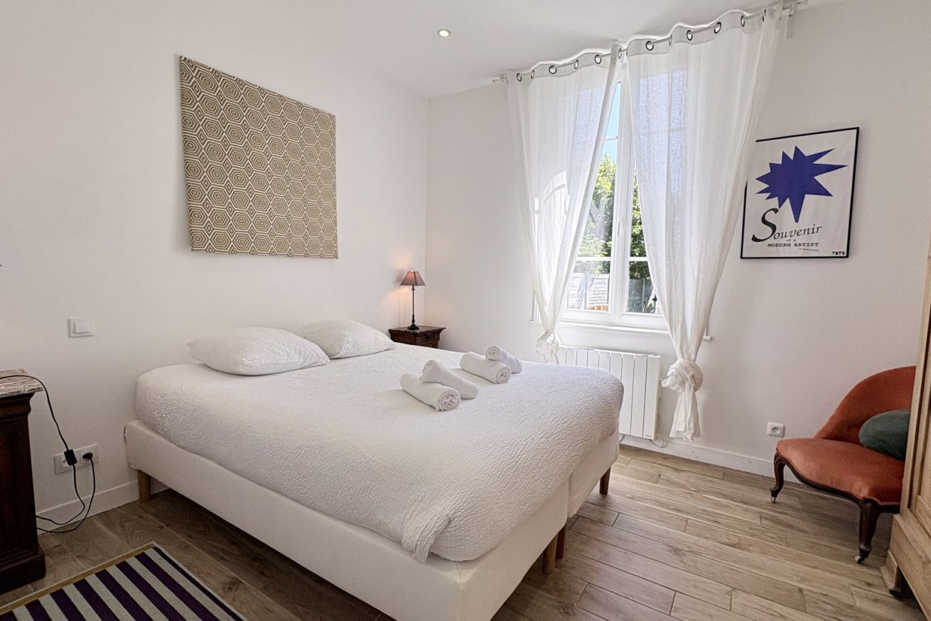 Une chambre à coucher avec un grand lit, une table de chevet, une lampe, une chaise et une fenêtre avec des rideaux.
