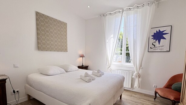 A bedroom with a large bed, a bedside table, a lamp, a chair, and a window with curtains.