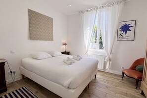 Une chambre à coucher avec un grand lit, une table de chevet, une lampe, une chaise et une fenêtre avec des rideaux.
