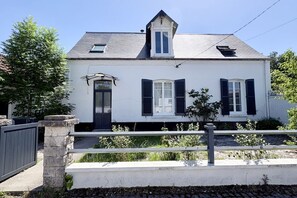 Une maison blanche avec des volets sombres, un petit porche et un mur en pierre.