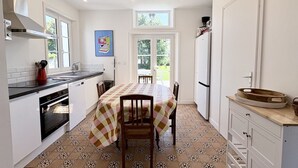 A kitchen with a dining table, chairs, a refrigerator, and a window.