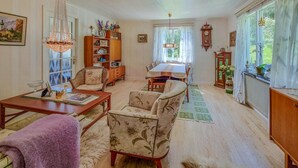 A cozy living room with a dining area, wooden furniture, and a large window with curtains.