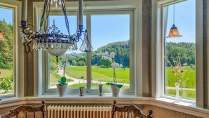 A dining area with a view of a green landscape through large windows, a chandelier, and a table with chairs.
