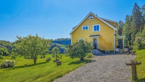 A yellow house with a porch, surrounded by a grassy landscape and trees.