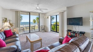 Ein Wohnzimmer mit Sofa, Couchtisch, Fernseher und einem Balkon mit Blick auf den Ozean.