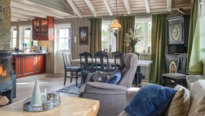 Ein gemütliches Wohnzimmer mit Kamin, eine Essecke mit Tisch und Stühlen sowie eine Küche mit Holzausstattung und Herd.