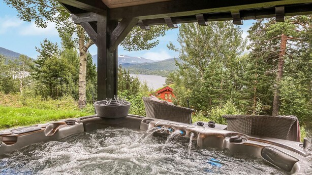 Ein Whirlpool mit fließendem Wasser, umgeben von Korbmöbeln und Blick auf einen See und Berge.