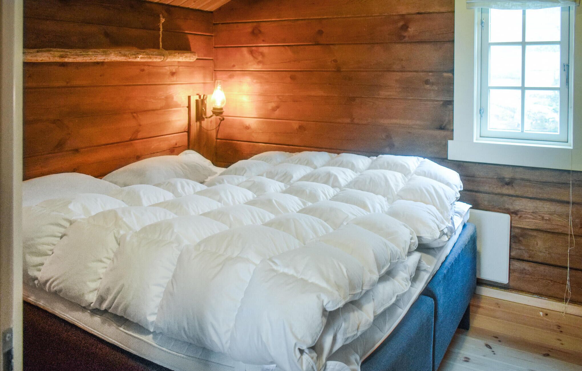 Quarto de cabana de madeira com uma cama, uma luminária na parede e uma janela.