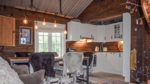 Interior rústico de una cabaña con paredes de madera, un comedor con mesa y sillas, y una cocina con armarios blancos.