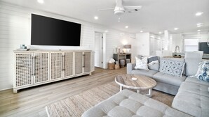 A modern living room with a grey sofa, a wooden coffee table, and a white entertainment unit with a flat-screen TV.
