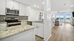 A modern kitchen with white cabinets, granite countertops, and a view of the ocean through large windows.