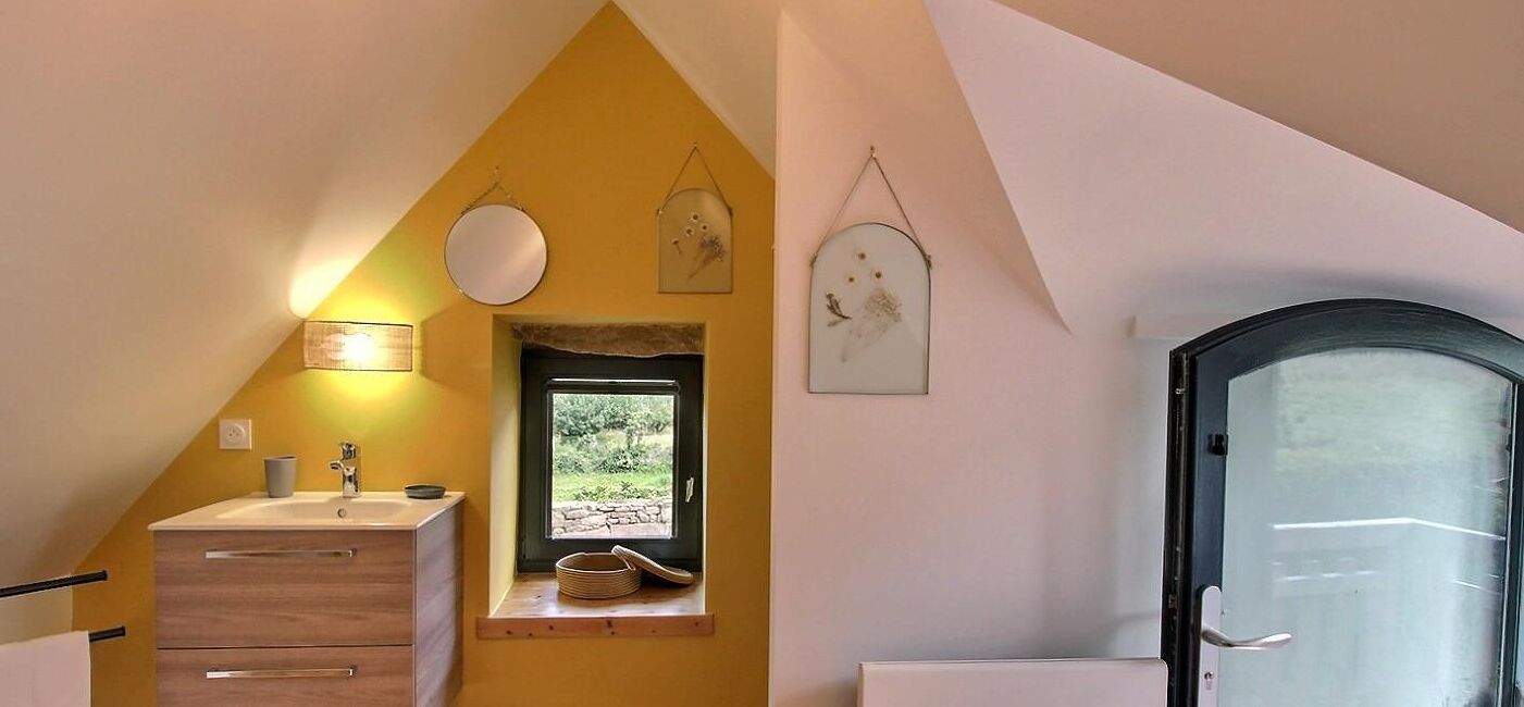 A small bathroom with a window, a sink, a mirror, and a door.