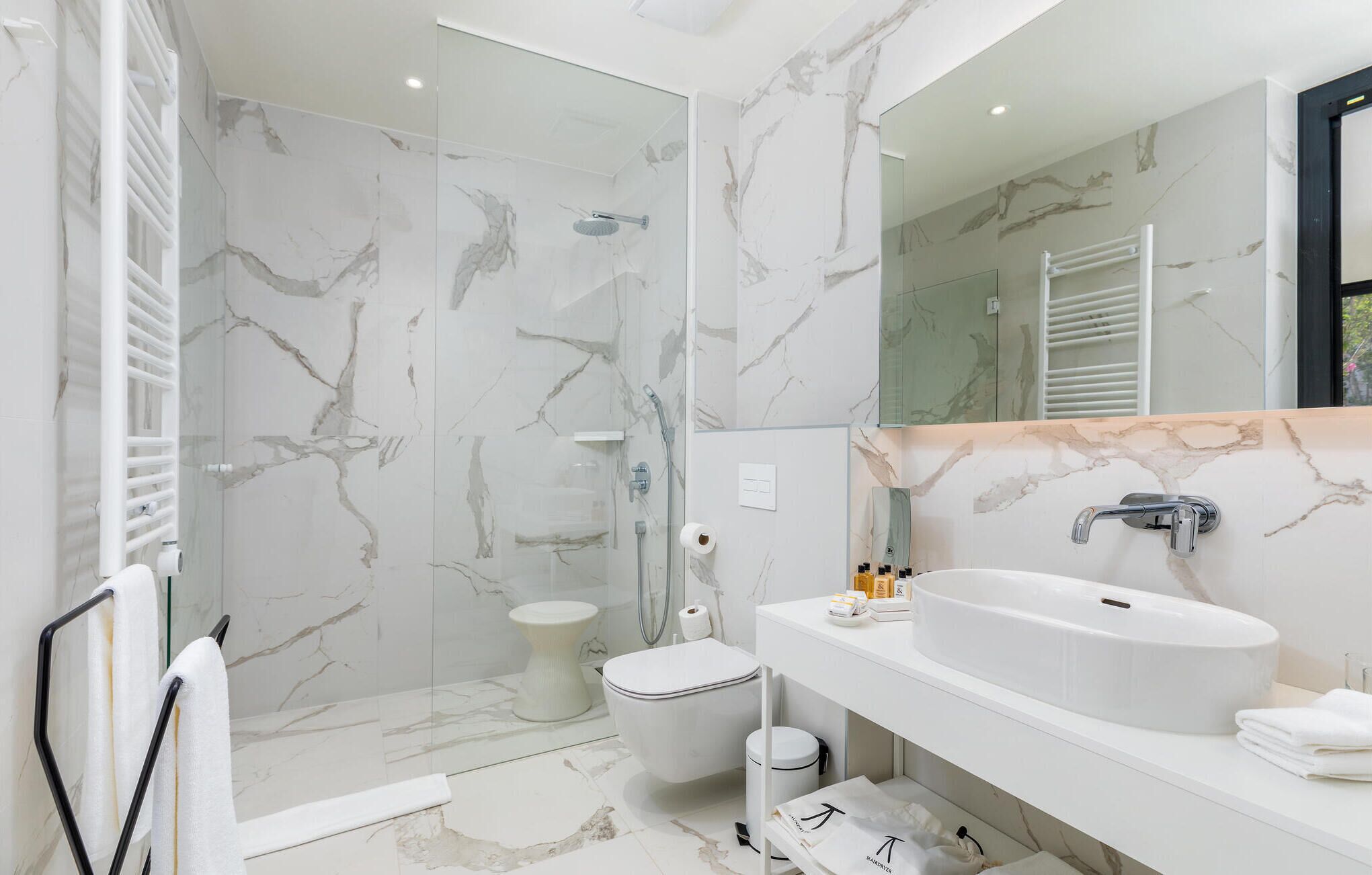 Ein modernes Badezimmer mit einer gläsernen Duschkabine, einem weißen Waschbecken und einer Wand mit Marmorfliesen.