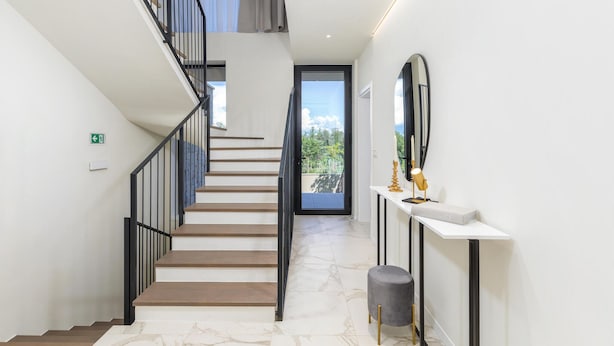 A modern interior with a staircase leading to a balcony, a white console table with a mirror, and a minimalist design.