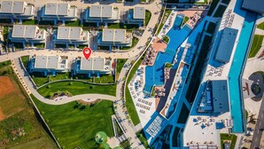 An aerial view of a modern hotel complex with multiple buildings, a central swimming pool, and a landscaped area with pathways.