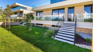 A modern two-story building with a glass facade, a stone base, and a well-maintained garden with grass and small trees.
