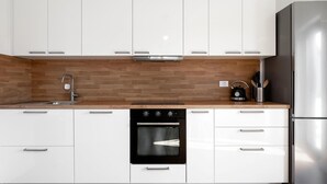 A modern kitchen with white cabinets, a wooden backsplash, stainless steel appliances, and a kettle on the countertop. - Lovely apartment in Brodarica with WiFi (Brodarica)