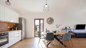 A modern kitchen with white cabinets, a wooden countertop, and a built-in oven. There is a dining area with a wooden table and chairs, a vase with flowers, and a flat-screen TV. - Lovely apartment in Brodarica with WiFi (Brodarica)