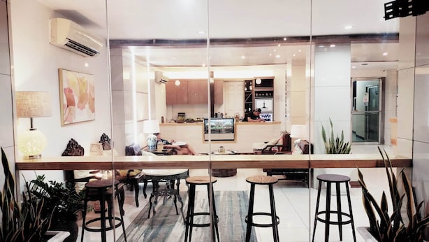 A modern hotel lobby with a reception desk, seating area, and a kitchen visible through the glass partition. - Fuente Pension House (Cebu)