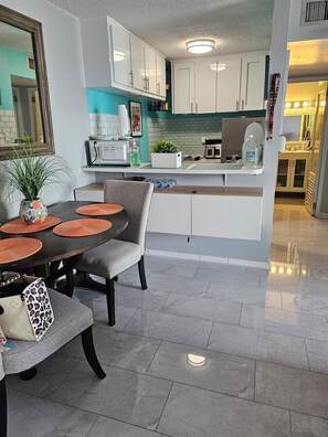 A modern kitchen with white cabinets, a dining area with a round table and chairs, and a small island with a microwave and a plant.