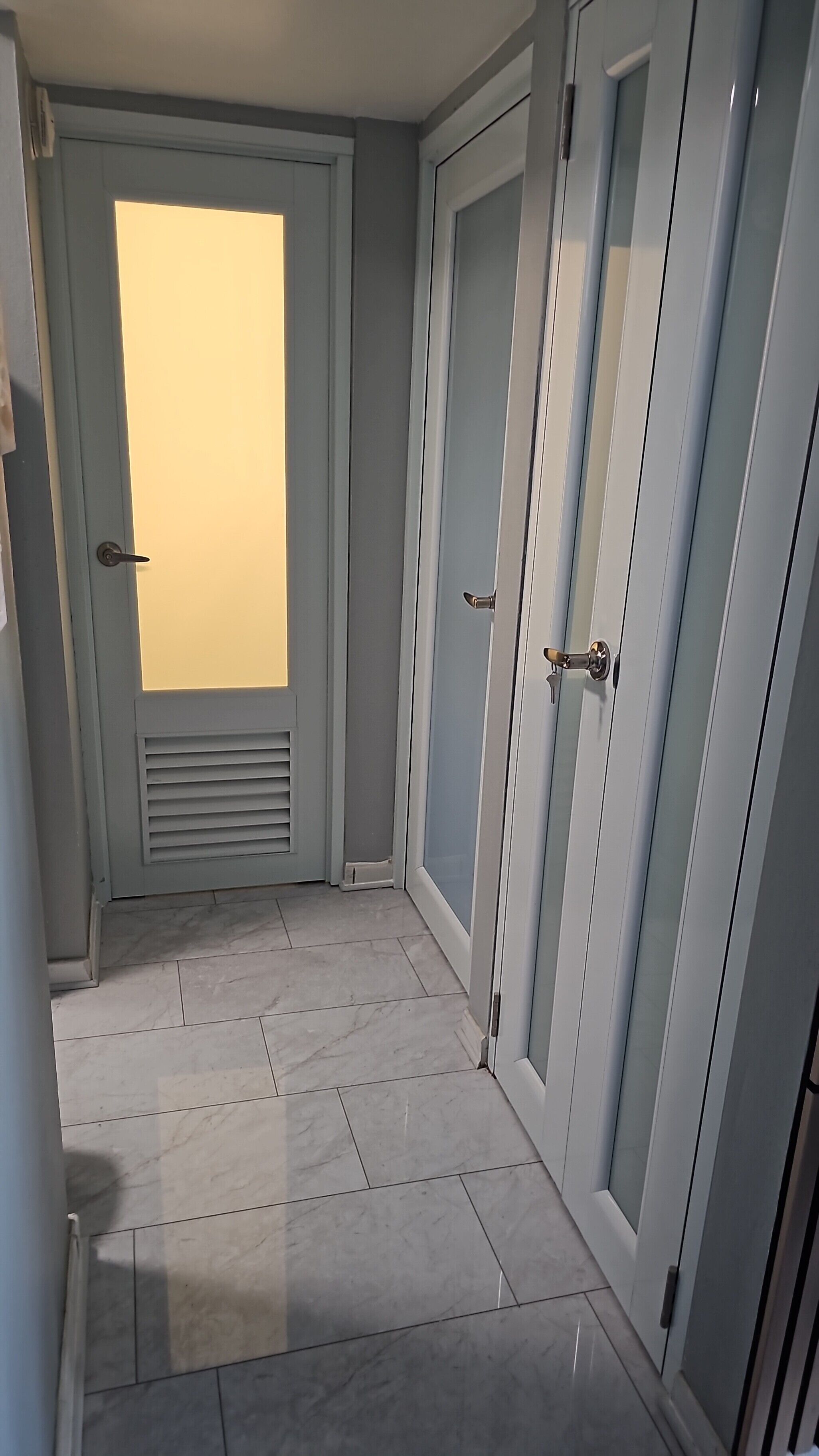 A hallway with a tiled floor, a door with a window, and a door with a handle.