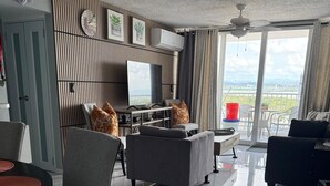 Una sala de estar moderna con un televisor de pantalla plana, sofás grises, una mesa de comedor y un balcón con vistas.