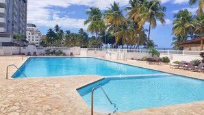Una piscina con solárium de piedra, rodeada de palmeras y una valla blanca.