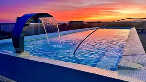 A pool with a waterfall feature and a view of the sunset.
