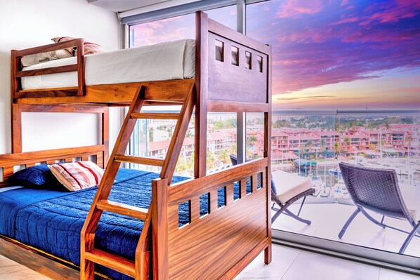 Cama individual en literas con vista a un paisaje urbano a través de ventanas amplias.