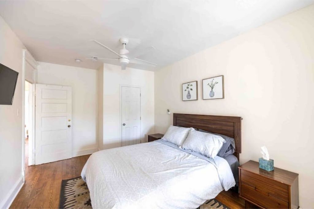 Ein Schlafzimmer mit einem Bett, einem Nachttisch, einem Deckenventilator und zwei gerahmten Bildern an der Wand.