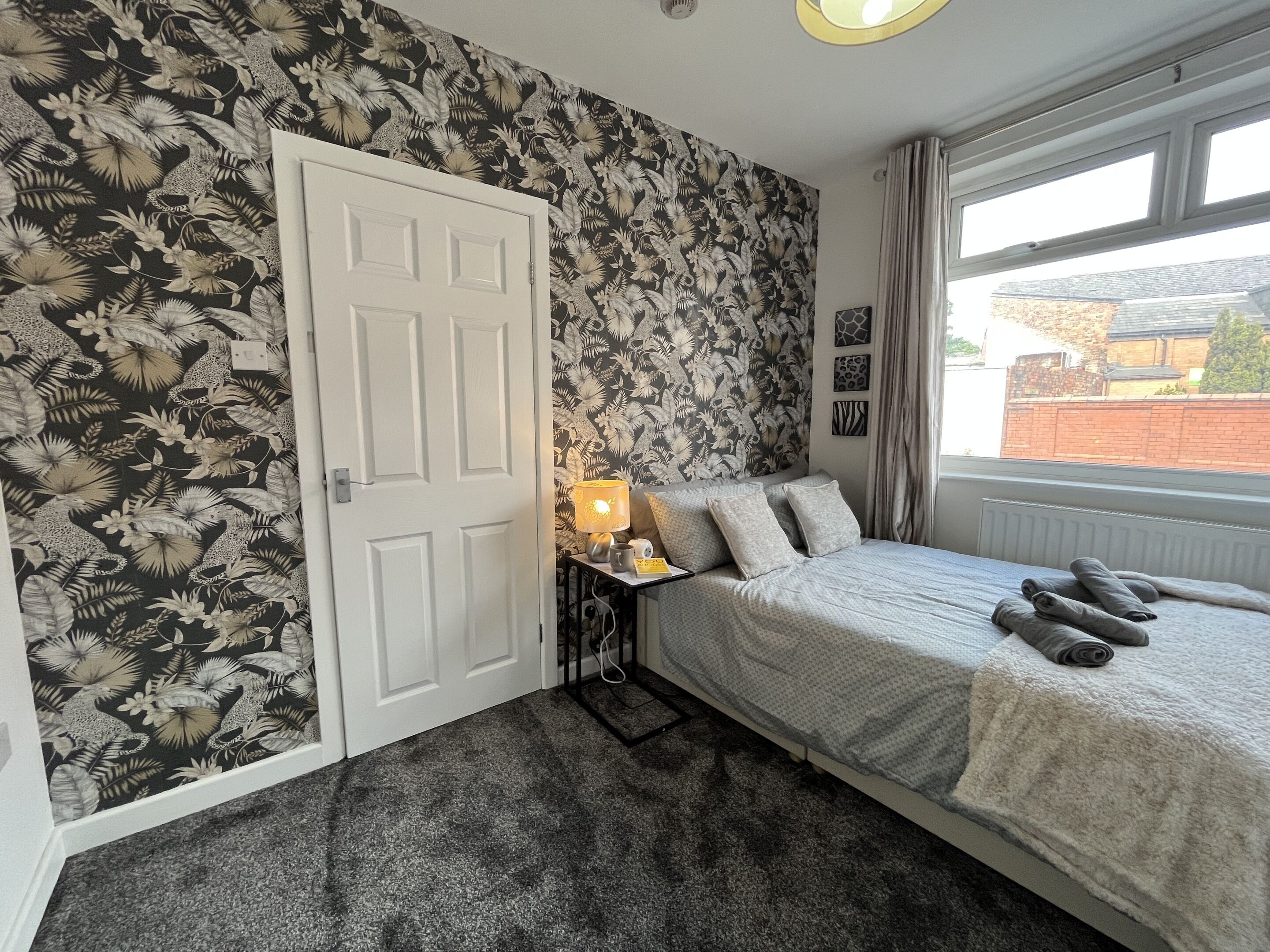 A bedroom with a bed, a nightstand with a lamp, a door, and a window with a view of the outside.