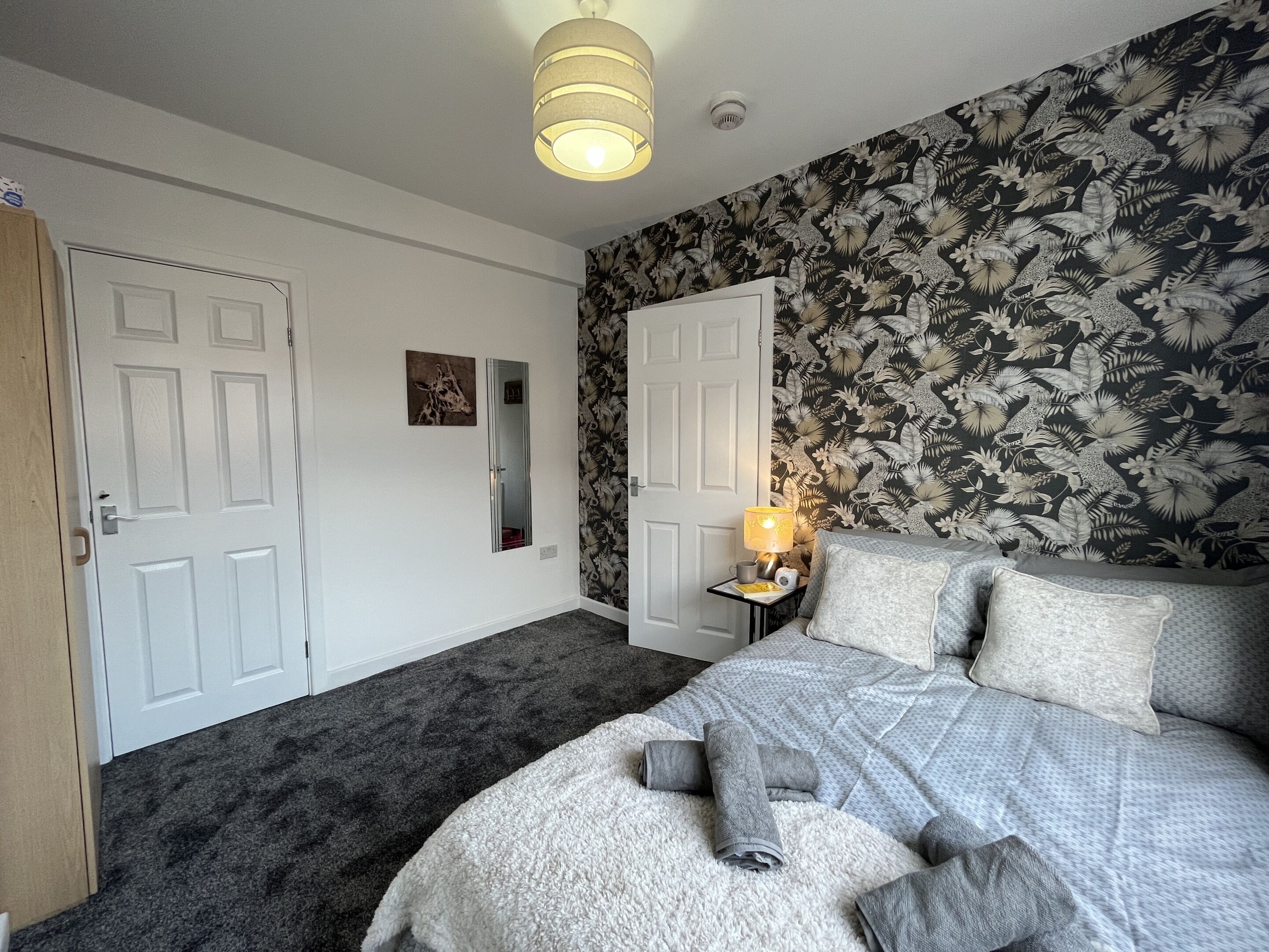 A bedroom with a bed, a nightstand, a lamp, and a door.