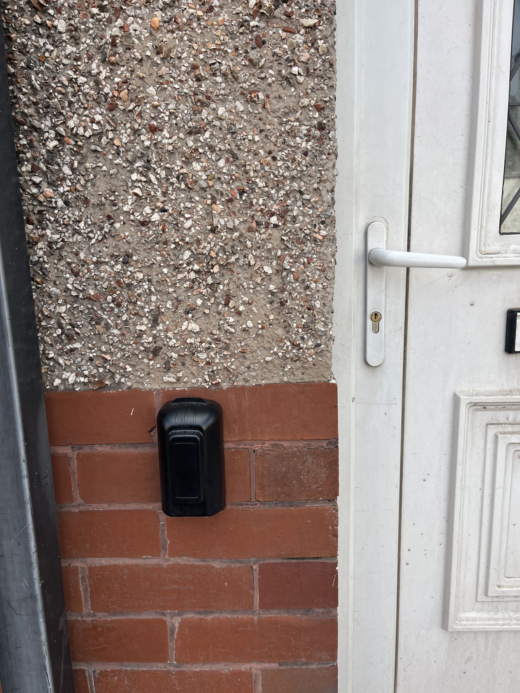 A door with a textured wall above it and a black intercom mounted on the brick wall.