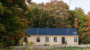 Une cabane en bois, dotée d’un toit sombre, entourée du feuillage automnal.